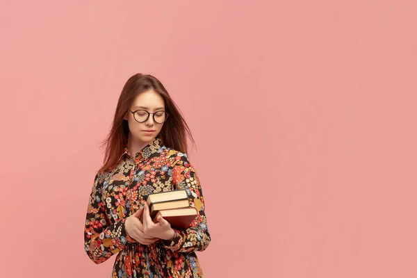 A young female student holds a stack of books in her hands and is going to learn English remotely while staying at home.