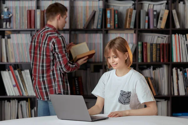 Drăguț băiat și fete studenți care lucrează la un proiect în biblioteca orașului, în căutarea de cărți și note de tastare pe un laptop . — Fotografie, imagine de stoc