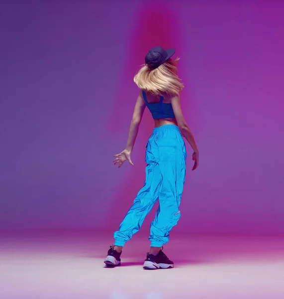 Aranyos tini lány táncol hip-hop reflektív nadrág, baseball sapka, egy stúdióban neon világítás. Táncszínes poszter. — Stock Fotó