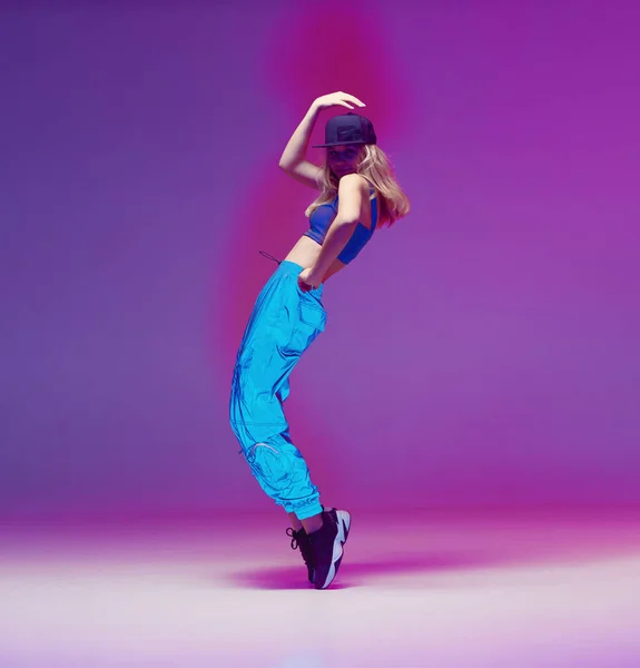 Aranyos tini lány táncol hip-hop reflektív nadrág, baseball sapka, egy stúdióban neon világítás. Táncszínes poszter. — Stock Fotó