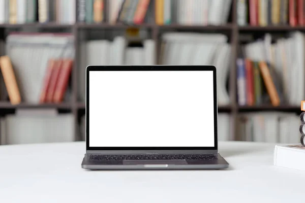 Un portátil con espacio de copia para texto se encuentra sobre una mesa en la biblioteca sobre el fondo de una estantería . —  Fotos de Stock