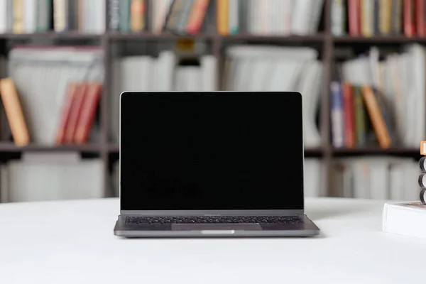 Un portátil con espacio de copia para texto se encuentra sobre una mesa en la biblioteca sobre el fondo de una estantería . —  Fotos de Stock