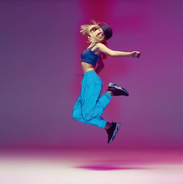 Yansıtıcı pantolonla, beysbol şapkasıyla neon ışıklı bir stüdyoda hip hop yapan tatlı bir genç kız. Dans rengi posteri.