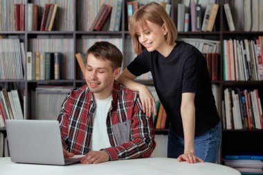 Şehir kütüphanesinde bir proje üzerinde çalışan sevimli erkek ve kız öğrenciler, kitap arıyorlar ve dizüstü bilgisayarlarında notlar yazıyorlar..