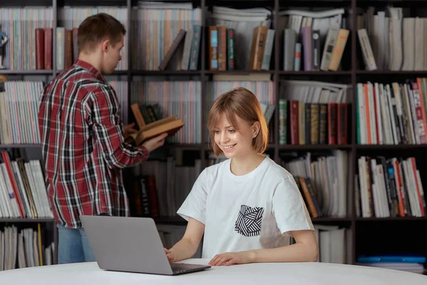 Drăguț băiat și fete studenți care lucrează la un proiect în biblioteca orașului, în căutarea de cărți și note de tastare pe un laptop . — Fotografie, imagine de stoc