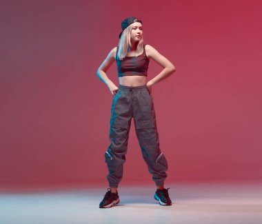 Stüdyoda neon ışıklı, şık kıyafetlerle hip-hop yapan, beysbol şapkası takan hoş bir genç kız. Dans rengi posteri.