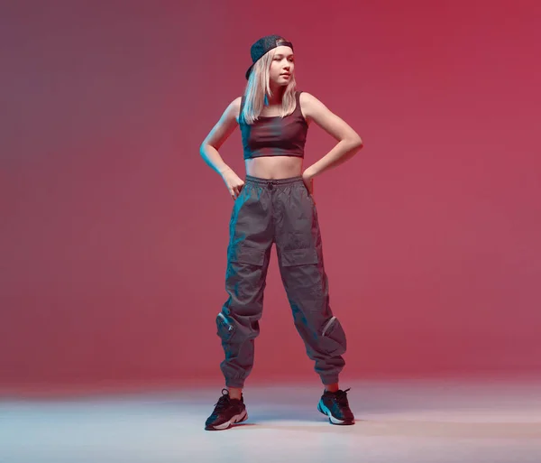 Nettes Teenie-Mädchen tanzt Hip-Hop in stylischer Kleidung, Baseballmütze, in einem Studio mit Neonbeleuchtung. Tanzfarbplakat. — Stockfoto