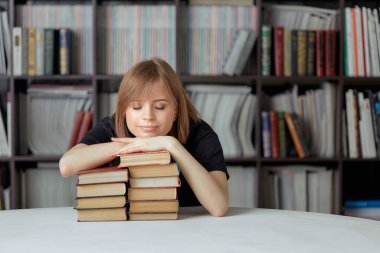 Havalı bir kız öğrenci kütüphanede oturuyor kitapların arkasına yaslanıyor..