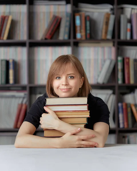 Egy menő diáklány ül a könyvtárban, könyvekre támaszkodva, egy könyvespolc hátterében.. — Stock Fotó