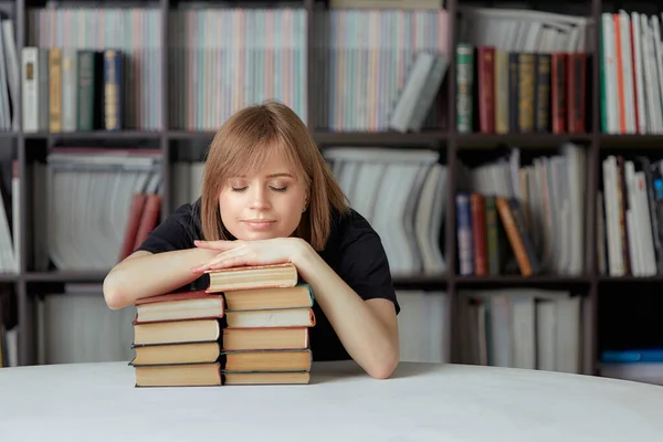 एक शांत लड़की छात्र किताबों पर झुका हुआ पुस्तकालय में बैठी है, एक किताब की शेल्फ की पृष्ठभूमि के खिलाफ . — स्टॉक फ़ोटो, इमेज