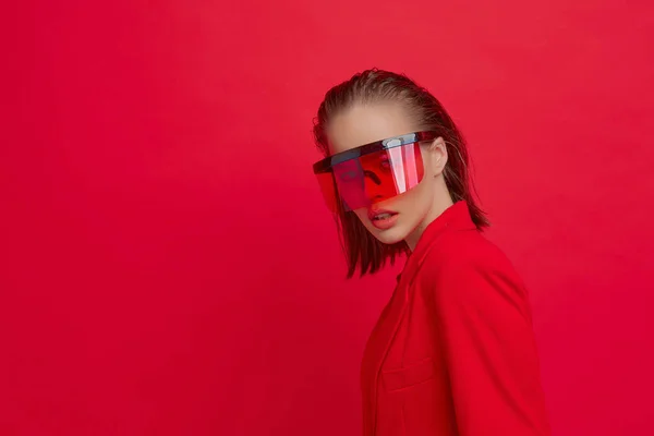 Chladná stylová dívka s módním účesem a stylovými brýlemi s velkým sklem pózuje na jasně červeném pozadí — Stock fotografie