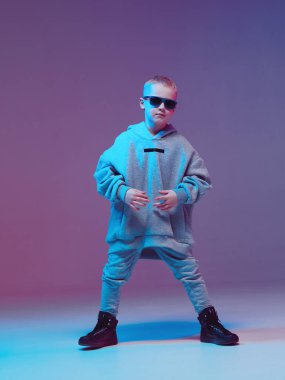 Kapüşonlu ve gözlüklü havalı çocuk, neon arka planda bir stüdyoda hip hop yapıyor..