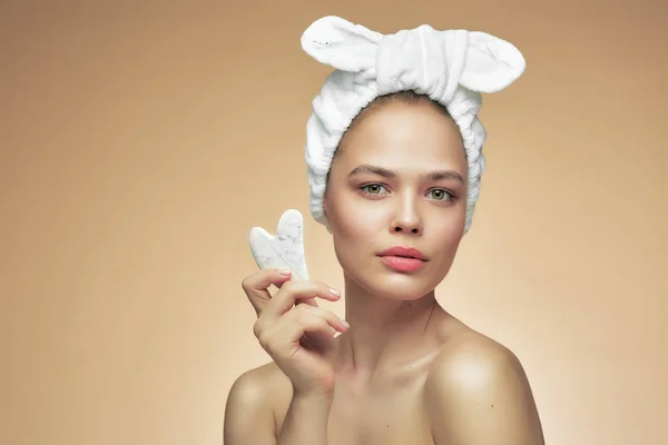 Vacker flicka med skönhet gua Sha kvarts sten för massage. Den beige bakgrunden är isolerad. Kosmetisk naturlig trend. — Stockfoto