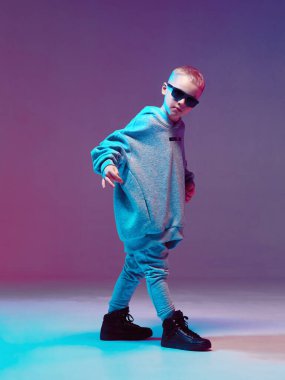 Kapüşonlu ve gözlüklü havalı çocuk, neon arka planda bir stüdyoda hip hop yapıyor..