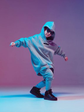 Kapüşonlu ve gözlüklü havalı çocuk, neon arka planda bir stüdyoda hip hop yapıyor..