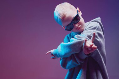 Rap yapan havalı bir çocuğun portresi, şık bir şekilde kapüşonlu, güneş gözlüklü ve neon arka planda poz veriyor..