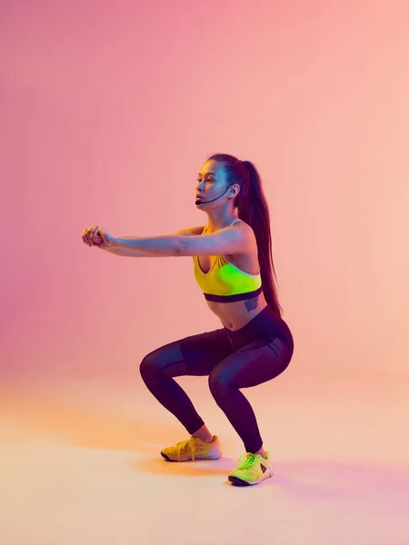 Athletic cool girl trainer teaches group crossfit and work out online training on a bright neon background.