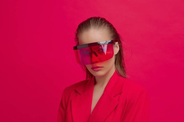 Havalı bir stil kızı, şık bir saç stili ve parlak kırmızı arka planda büyük cam pozlar veren şık gözlükleri var.