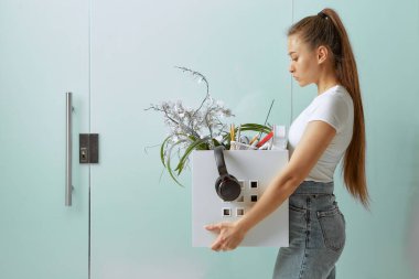 Genç ve güzel bir kız, kriz nedeniyle işten çıkarılıp kovulduktan sonra bir kutuda ofis malzemeleriyle yürüyor..