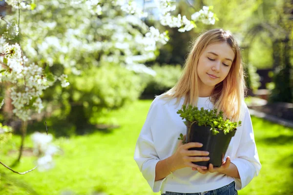 Seorang gadis bahagia dan manis sedang mempersiapkan untuk menanam bunga di kebun rumahnya di teras sebelah pohon Apple mekar. — Stok Foto