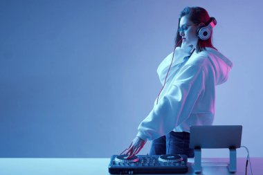 Havalı genç kız DJ karışık konsol ve dizüstü bilgisayarda müziği karıştırıyor, şık kıyafetler içinde, neon arka planda gözlük takıyor..