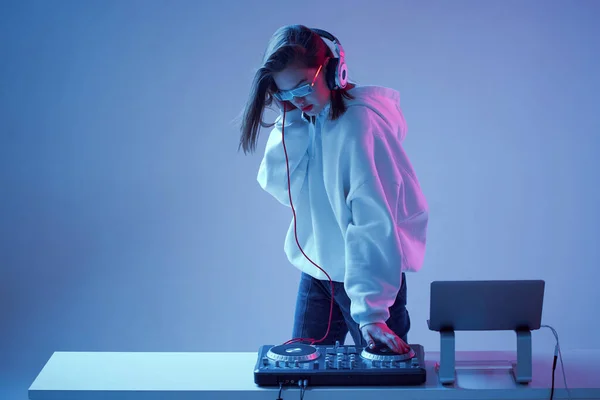 Havalı genç kız DJ karışık konsol ve dizüstü bilgisayarda müziği karıştırıyor, şık kıyafetler içinde, neon arka planda gözlük takıyor.. — Stok fotoğraf