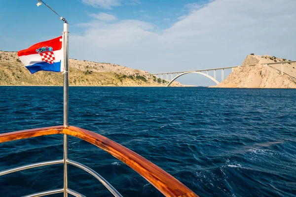 Güneşli bir yaz gününde Krk adasına giden köprü mavi gökyüzünün altında. Krk, Hırvatistan 'ın Adriyatik Denizi kıyısındaki büyük bir adadır. Seyahat arazisi. Gemiden çekilmiş bir fotoğraf. Sol tarafta Hırvat bayrağı