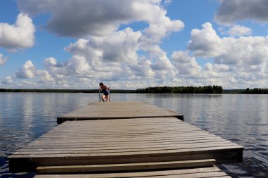 Genç kız (14), sıcak bir yaz gününde Ranua, Lapland, Finlandiya 'daki Ranuanjarvi Gölü' nde, su damlatan bir iskelede merdivene tırmanıyor..  