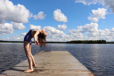 Genç bir kız (14), sıcak bir yaz gününde Ranua, Lapland, Finlandiya 'daki Ranuanjarvi Gölü' ndeki ahşap bir rıhtımda geriye doğru eğiliyor..  