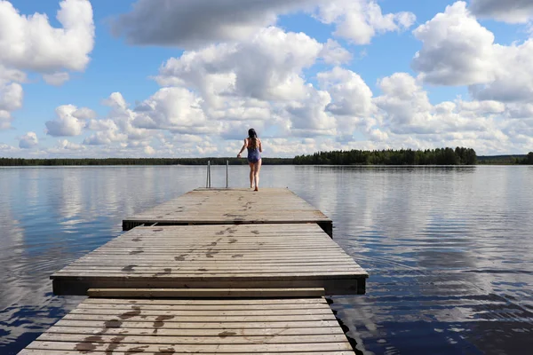 Teenage girl (14) midair as she runs off the end of a wooden pier at Lake Ranuanjarvi in Ranua, Lapland, Finland on a warm cloudy summer day.