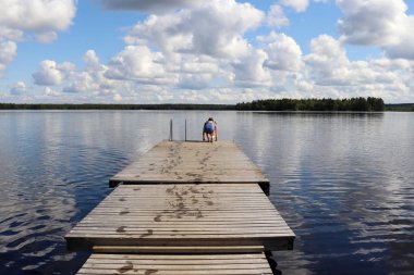 Genç bir kız (14), sıcak bir yaz gününde Ranuanjarvi Gölü, Laponya, Finlandiya 'daki ahşap bir iskeleden atlamaya hazırlanıyor..  