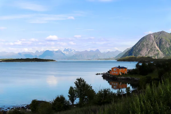 Norveç 'teki Lofoten Adaları' nın arka planında mavi dağları olan mavi gölün kıyısındaki turuncu ev..