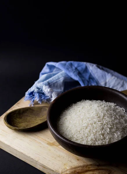 Uncooked rice in clay bowl on a wooden table with black background.