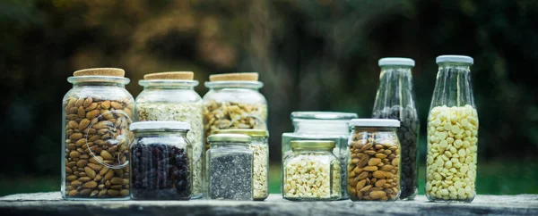Dried apple, chia seeds, almonds, nuts, seeds, oats in glass jars with nature background, on a wooden table. Healthy food concepts. Vegan concept.