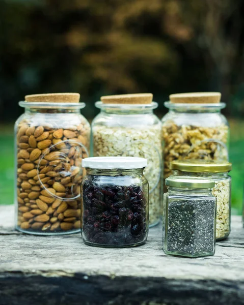 Nuts, seeds, oats in glass jars with nature background, on a wooden table. Healthy food concepts. Vegan concept.