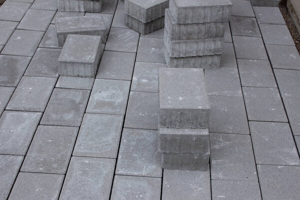 Бетонные тротуарные блоки укладываются рядом со зданием, некоторые тротуарные камни укладываются для дальнейшего использования
