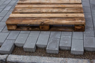 Bir binanın yanında beton kaldırım taşına yer bırakarak beton kaldırım taşları döşenmiş. Yeni kaldırımda boş bir ahşap palet duruyor.