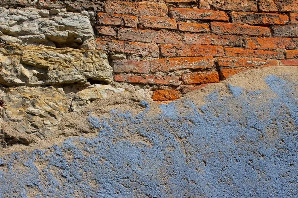 Old and weathered natural stone and brick wall with light blue paint plaster fallen off on on one side for background