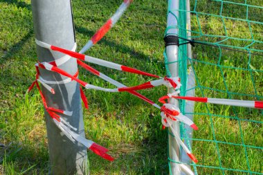 Futbol kalesi ve metal bir direğe bağlı kırmızı ve beyaz bariyer bandı, futbol veya futbol sahası kavramı kordemiye kapalı