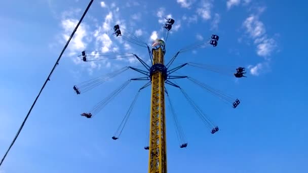 Spinnen op de merry-go-round in attractiepark hoog boven de grond op de blauwe hemelachtergrond op zonnige dag mensen — Stockvideo