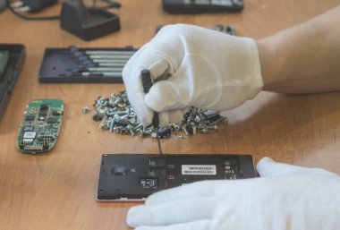 tamir teknisyeni beyaz eldiven tarafından mobil cep telefonu zarar görmüş. Sadece masanın üzerinde görünür eller