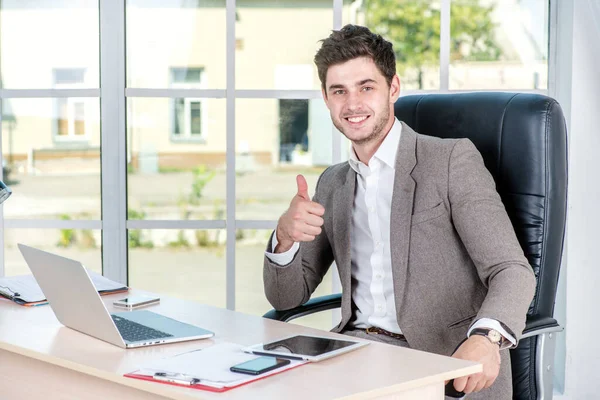 Confident businessman sitting in the office and show thumbs up. Businessman making successful business.