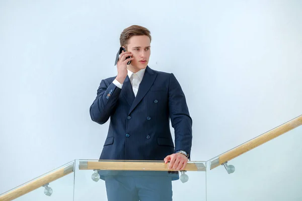 Conversation with the client. Successful businessman standing on the stairs and talking on a cell phone in a business office while looking forward. Businessman in formal wear.