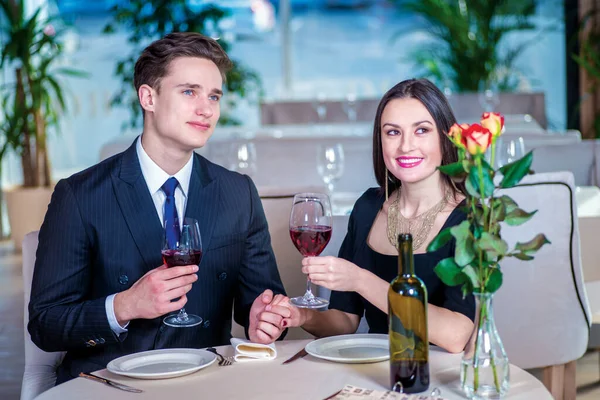 Gala dinner for two. Romantic dinner in the restaurant. Young loving couple visits a restaurant and raised their glasses of wine and look out the window until the guy holding the hand of a woman