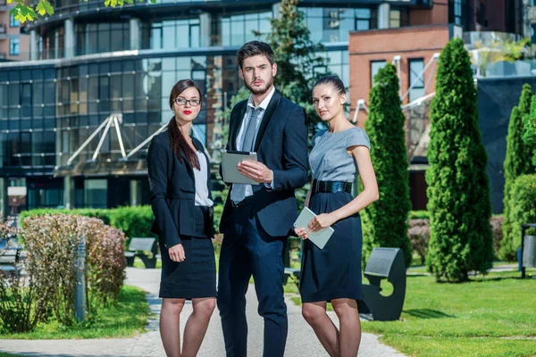 The best workers. Three successful business people in formal clothes standing on the street to discuss business and keep computers in their hands. Young businessman smiling and looking at the camera