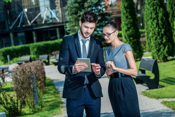 Checking job. Smiling businessman and successful businesswoman in formal clothes standing on the street and discuss business matters. Young businessman holding a tablet in his hands