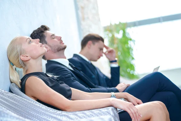 Tired from work. Tired businessman sitting in board room and bowed head back to rest. Businesspeople sitting in a line and dressed in formal wear.