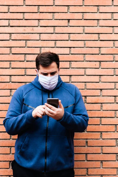 Adam tıbbi bir maskeyle cep telefonuna dokunuyor..