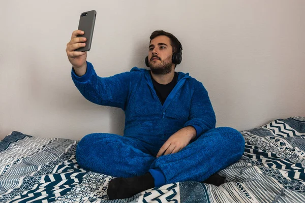 Yatak odasında pijamalı komik bir genç adam. Müzik dinlerken selfie çekiyor..