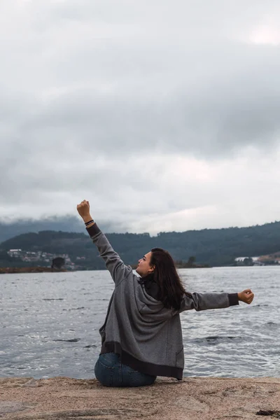 Kadın deniz kıyısında otururken hem görüyor hem de dinleniyor. Kollarını kaldırıyor..